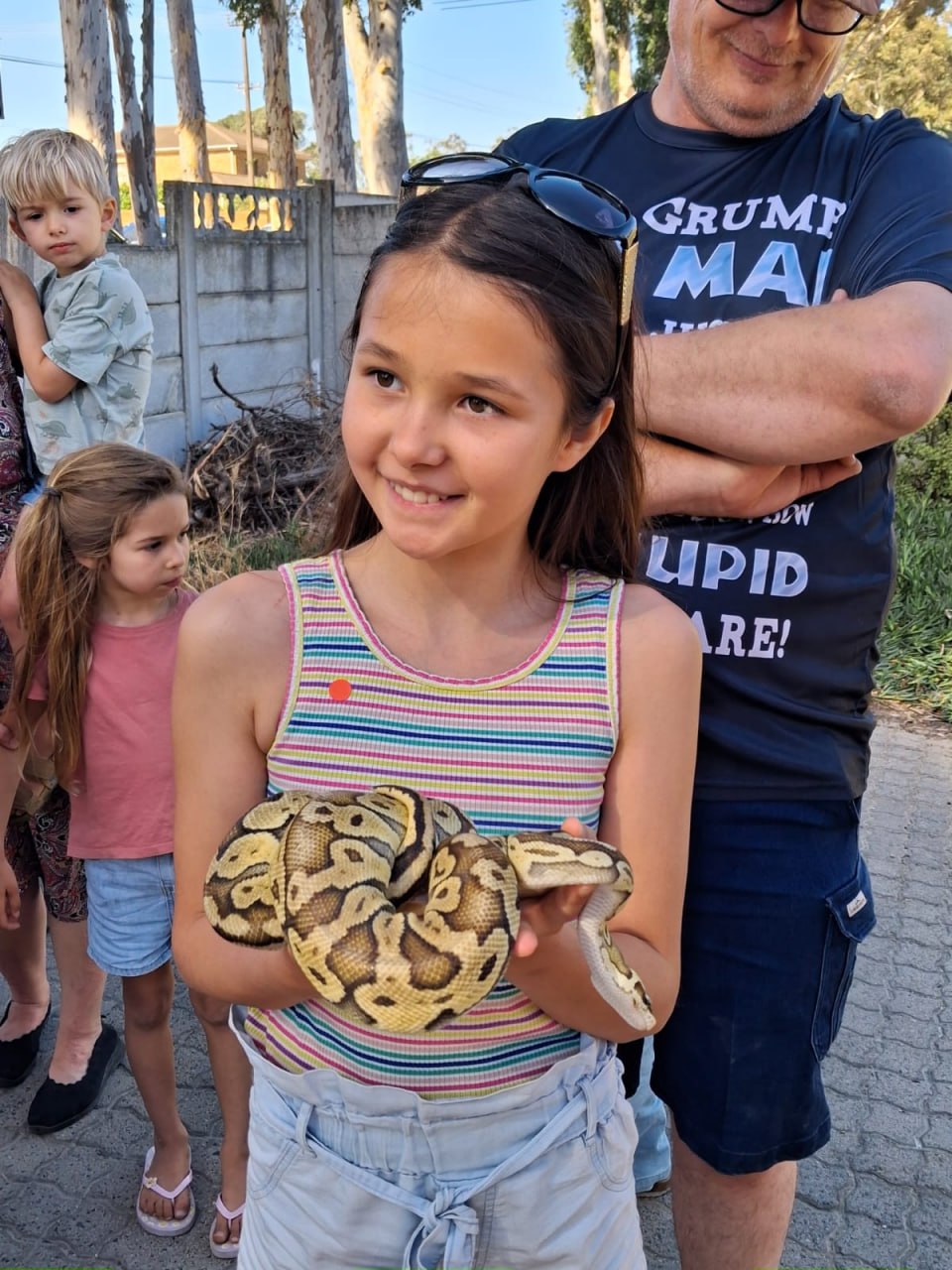 A girl holding a pastel ball python, with an older man and other children behind her, at the Penhill Snake Show