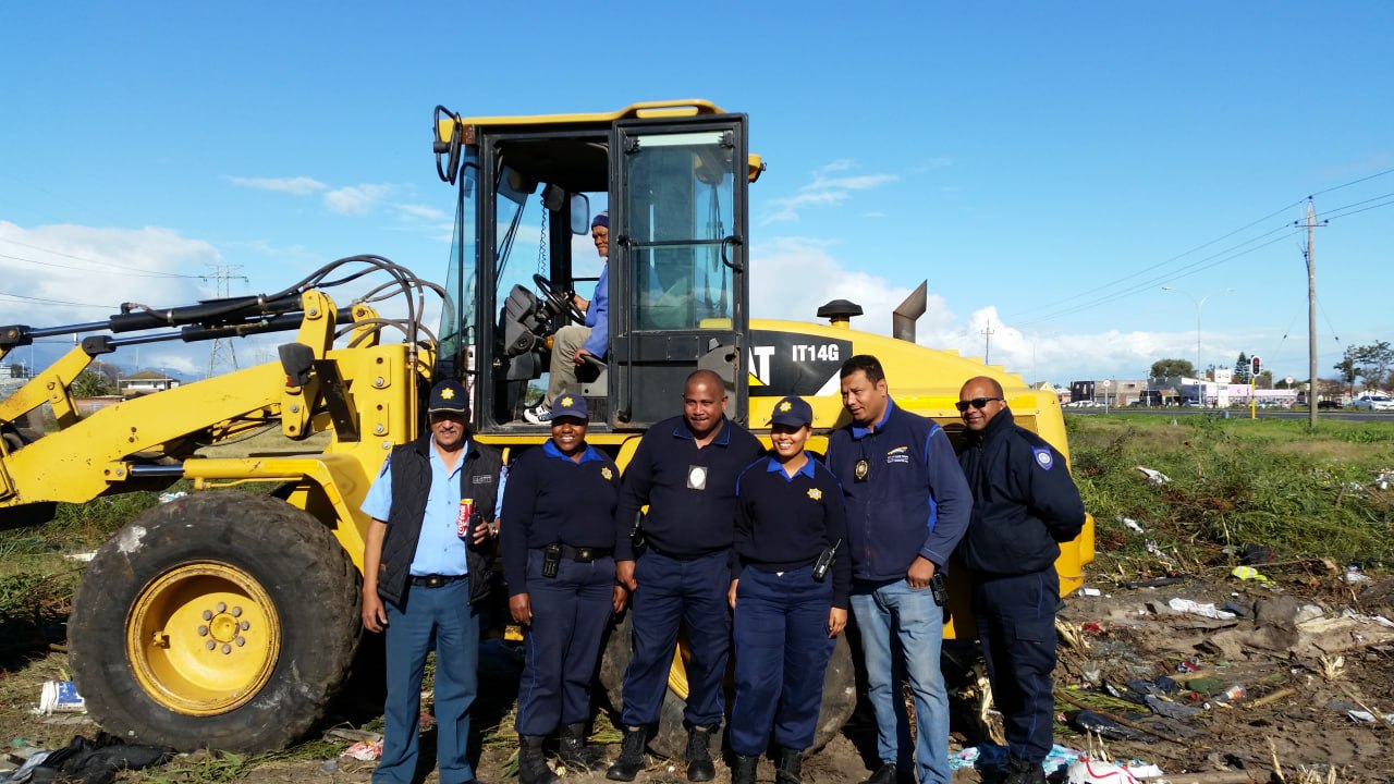 Law enforcement and community safety officers with a CAT front-end loader during the bush-clearing operation