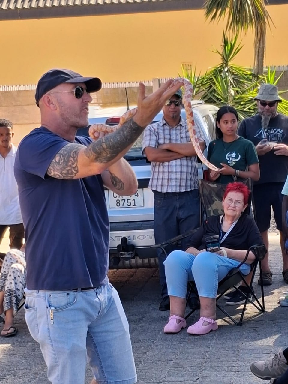 Handler holding up a slender, tan-and-orange blotched snake for the crowd at the Penhill Snake Show